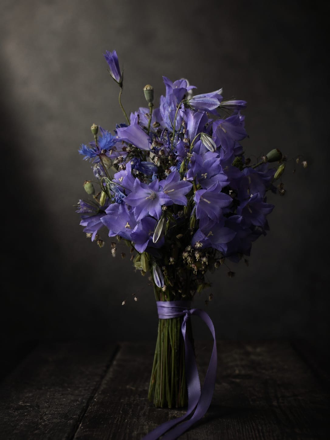 Violetter Blumenstrauß mit Schleife auf dunklem Holztisch